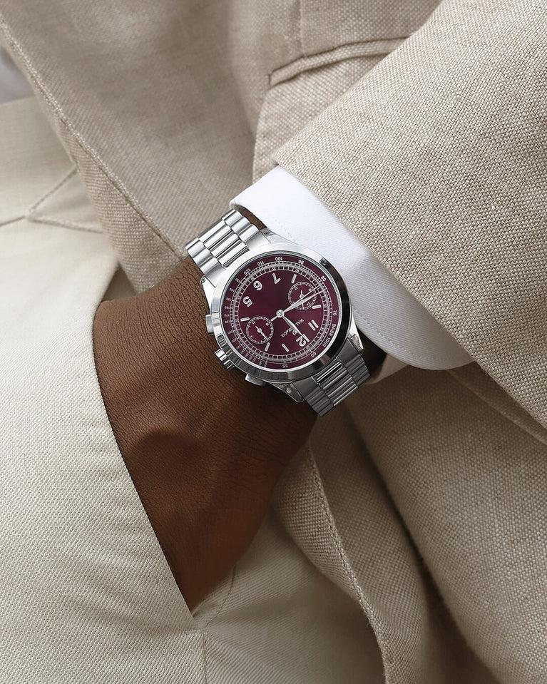 A round mens watch in rhodium-plated silver from Waldor & Co. with a burgundy colored sunray dial and a second hand. Seiko movement. The model is Chrono 39 Porto Cervo.