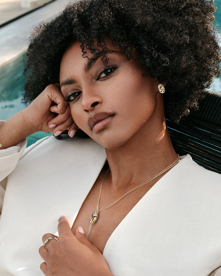 A polished stainless steel ring in 14k gold from Waldor & Co. One size. The model is Dual Knot Ring.