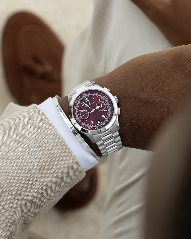 A round mens watch in rhodium-plated silver from Waldor & Co. with a burgundy colored sunray dial and a second hand. Seiko movement. The model is Chrono 39 Porto Cervo.