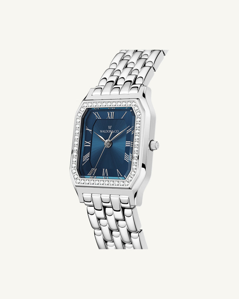 A square womens watch in Rhodium-plated 316L stainless steel from Waldor & Co. with dark blue dial. Bezel with premium crystals. Diamond Cut Sapphire Crystal glass dial. Seiko movement. The model is Eternal 22 Bellagio Pavè.
