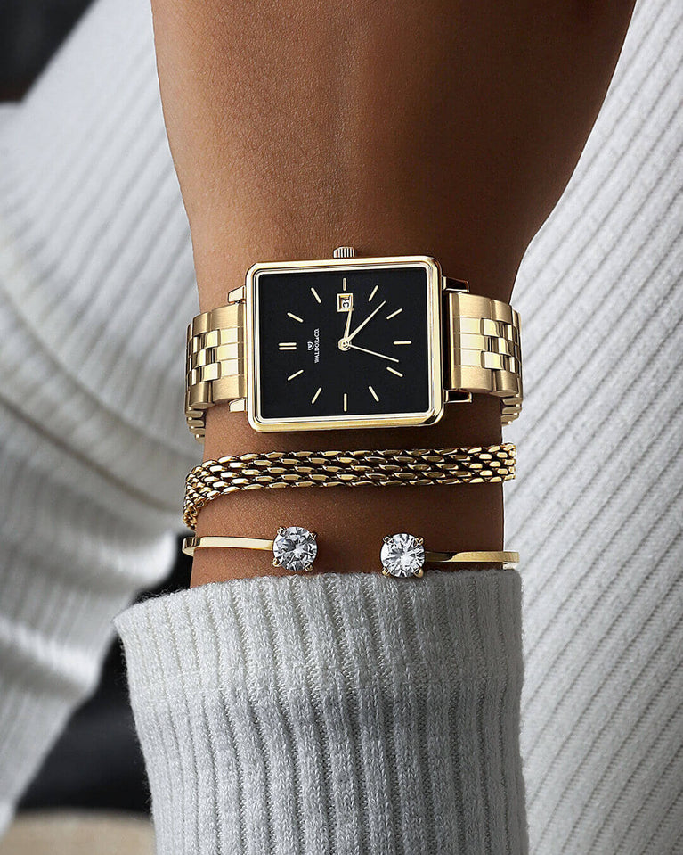 A square womens watch in 14k gold from Waldor & Co. with black sunray dial and a second hand. Seiko movement. The model is Delight 32 Chelsea 28x32mm.